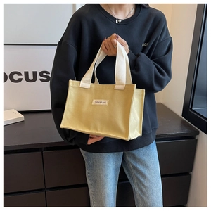 Détail du sac fourre-tout en toile jaune avec écusson FASHIONS BAG tenu par un mannequin