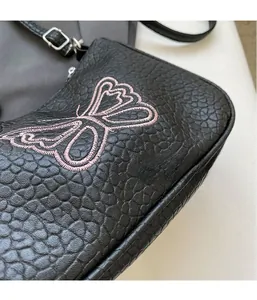 Gros plan du sac bandoulière en cuir grainé noir avec broderie de papillon rose