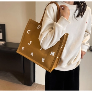 Close-up of a large capacity canvas tote bag in mustard yellow with bold white letters