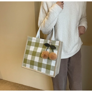 Detail of green and white checkered linen tote bag with brown plush cherry charm