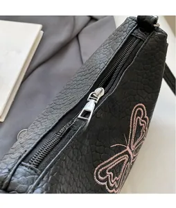 Détail du sac en cuir grainé avec broderie papillon rose et fermeture éclair en métal
