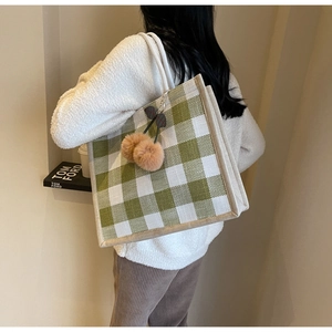 Detail of green checkerboard linen tote bag with plush cherry charm on female model