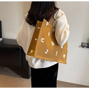 Mustard yellow canvas tote bag with bold white lettering shown on a model for daily use