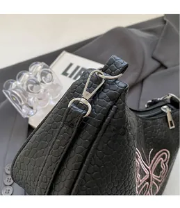 Détail des crochets en métal argenté et broderie papillon rose sur sac en cuir embossé noir