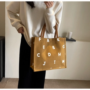 Detail of yellow canvas tote bag with brown rope handles and stylish white letter print