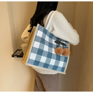 Side view of a blue and white checkered linen tote bag with cherry pompom charm on model