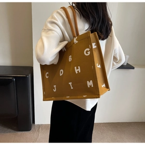 Detail of a large yellow canvas tote bag with letter print worn over the shoulder