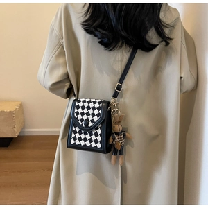 Close-up of a tweed crossbody phone bag with a cute plush rabbit charm on a trench coat
