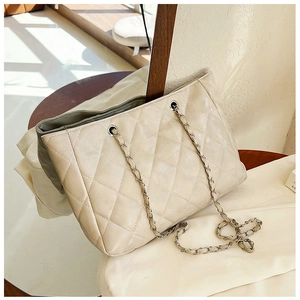 Detailed view of beige quilted tote bag with silver chain strap and diamond pattern