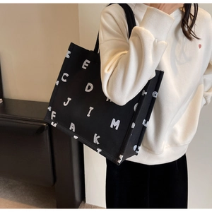 Side view of black canvas tote bag with white letters worn by a female model