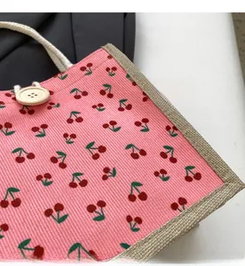 Detail of pink corduroy handbag with cherry print, wooden button and braided handles