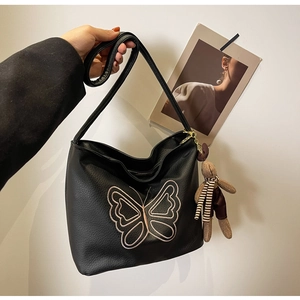 Detail of black lychee texture tote bag featuring pink butterfly embroidery and rabbit charm