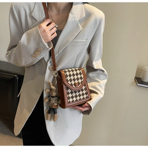 Brown checkered woven crossbody bag with a cute rabbit pendant shown on a model