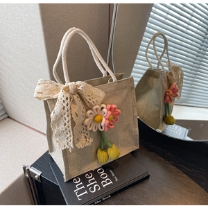 Close-up of beige linen woven tote bag with white lace bow and floral knitting charm