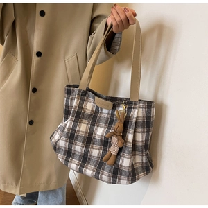 Detail of plaid wool tote bag with brown leather straps and a cute knit bear pendant