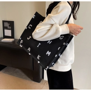 Detail of a large black canvas tote bag with white letter print worn by a model