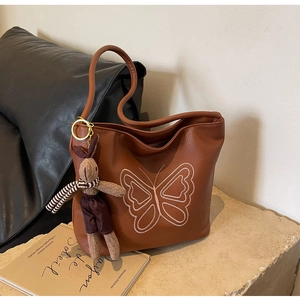 Close-up of brown pebble leather tote bag featuring pink butterfly embroidery and rabbit charm