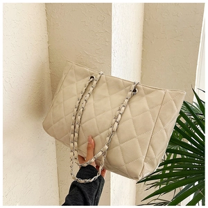 Detail of quilted leather texture and golden chain strap on large ivory tote bag