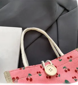 Detail of pink corduroy handbag with red cherry patterns and rustic wooden button