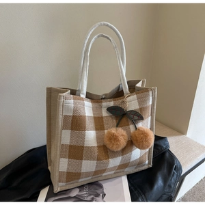Detail of linen tote bag with gingham pattern, cherry pompom charm, and magnetic closure