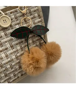 Close-up of plush cherry keychain with faux fur balls and green leather leaves on a bag