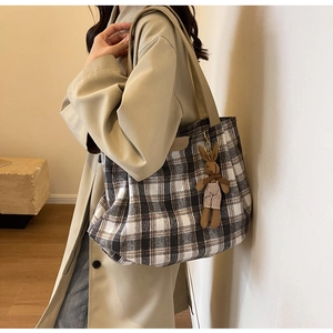 Side view of checkered canvas tote bag with brown leather handles and rabbit charm