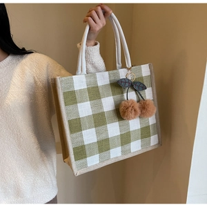 Close-up of green waffle pattern tote bag with plush cherry charm and woven handles