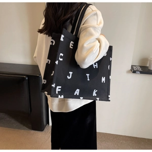 Detailed side view of a large black canvas tote bag with white letter print on model