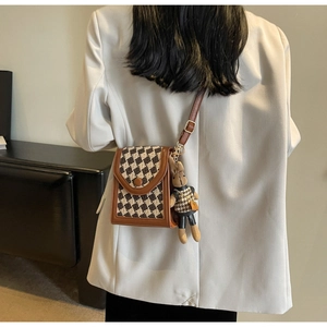 Detail of a vintage checkered crossbody bag with rabbit plush charm on a model