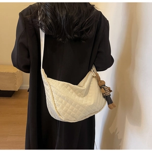 Vue arrière du mannequin portant un sac matelassé beige avec un charm d'ours