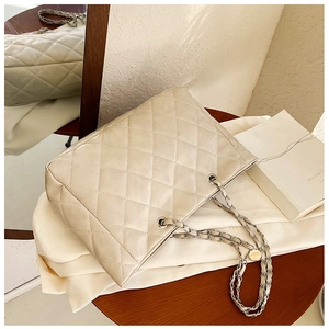 Detail of beige quilted tote bag featuring a leather-threaded silver chain on wooden table