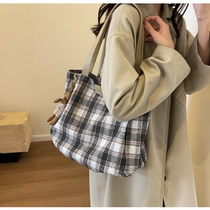 Detail of vintage plaid tote bag with brown leather straps and a plush bear pendant