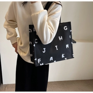 Detail of a large black canvas tote bag with white letter print and durable shoulder straps