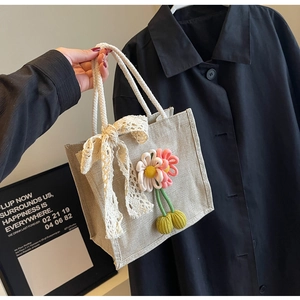 Detail of beige canvas lunch bag with lace bow and plush floral cherry keychain