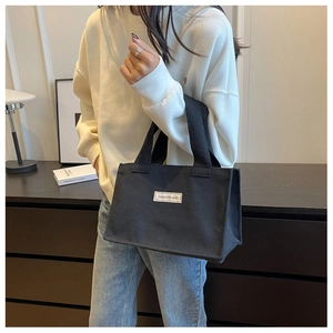 Détail du sac cabas en toile noire montrant l'étiquette blanche et la poignée tissée robuste