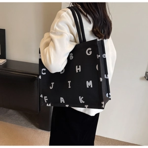Close-up of a large black canvas tote bag with white letter prints on a shoulder model