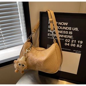 Détail d'un sac jaune avec broderie de nœud rose et pendentif de monstre en peluche marron