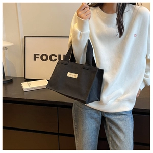 Détail du sac cabas en toile noire avec étiquette tissée porté par un mannequin