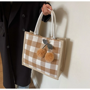 Detail of checkered linen tote bag with decorative cherry pom-poms and rope handles