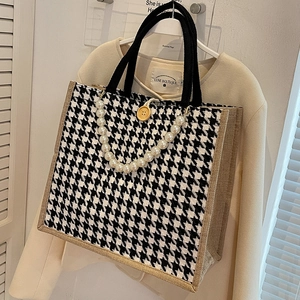 Large houndstooth tote bag with jute trim and pearl strap detail on a beige blazer