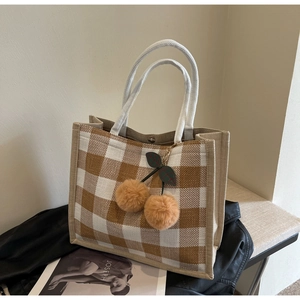 Detail of waffle plaid tote bag featuring a plush cherry charm and thick handle