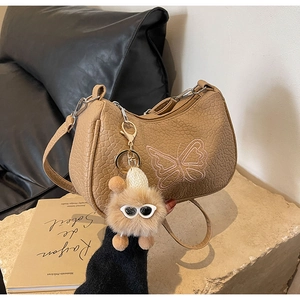 Détail du sac en cuir kaki avec broderie papillon rose et pendentif en peluche assorti