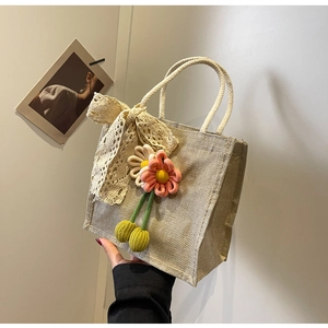 Close-up of jute tote bag featuring pink knit flowers and a lace bow handle detail