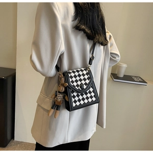 Detail of a checkered crossbody bag featuring a brown plush rabbit charm and adjustable strap