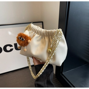 Detail of cream pleated cloud bag featuring gold chain strap and brown monster plush charm