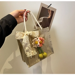 Detail of jute tote bag with white lace bow and handmade knitted flower pendant