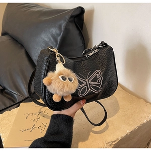 Détail du sac à main en cuir grainé noir avec broderie papillon rose et pompon décoratif