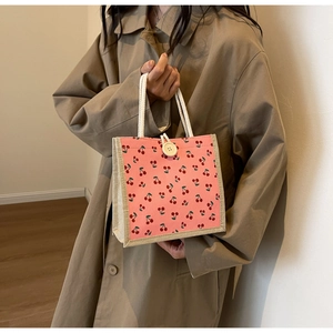 Detail of pink canvas tote bag featuring cherry patterns and white rope handle