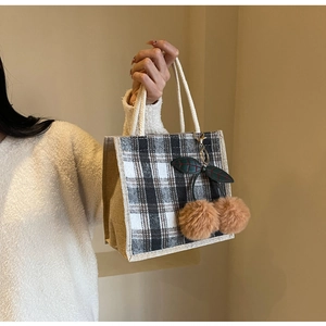 Detail of checkered canvas tote bag featuring cherry pom-pom charms and braided rope handles