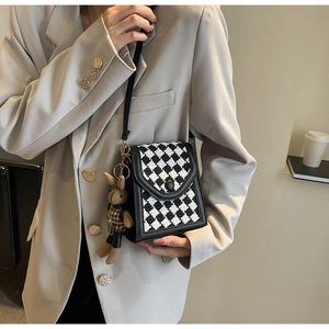 Detail of checkered woven phone bag with leather trim and brown plush bunny pendant